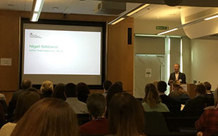 Nigel Gibbens speaking to a room of people. Large screen at the front of the room depicts his name.