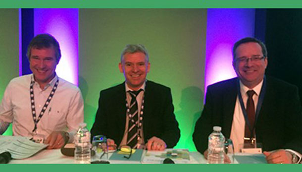 Co-chairs Thijs Kuiken, Ian Brown and David Swayne sitting at a desk lit up by purple lights against a green background.