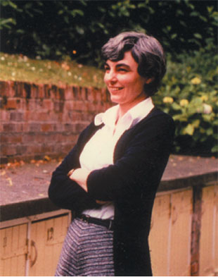 Margaret Lucas, standing with her arms folded, looking away from camera and smiling.