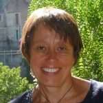 Image of a lady smiling at the camera with trees in the background.