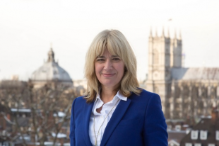 Image of a lady wearing a blue blazer over a white shirt looking at the camera with a London city-scape in the background, including the Houses of Parliament.