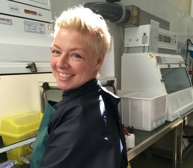 Female veterinary investigation officer standing in a lab at a glass cabinet with a surgical knife in her hand