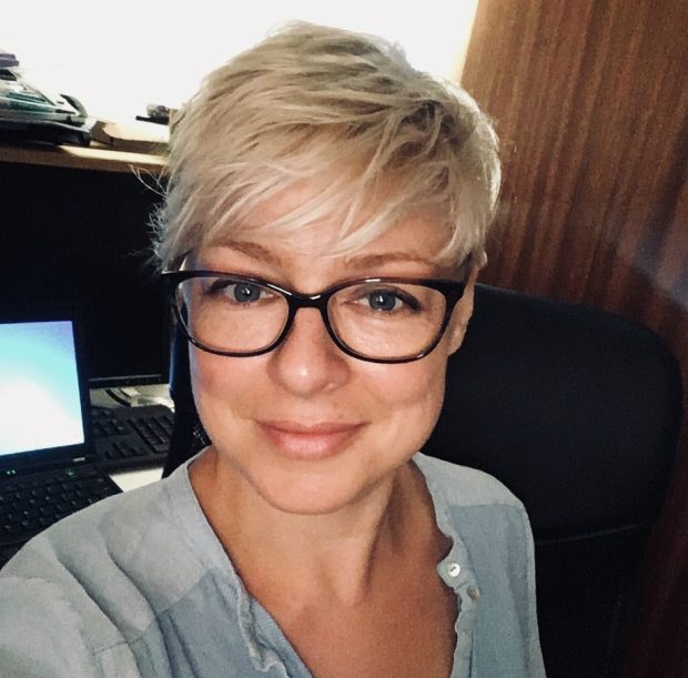 Female veterinary investigation officer wearing glasses looking into the camera with a laptop screen showing in the background