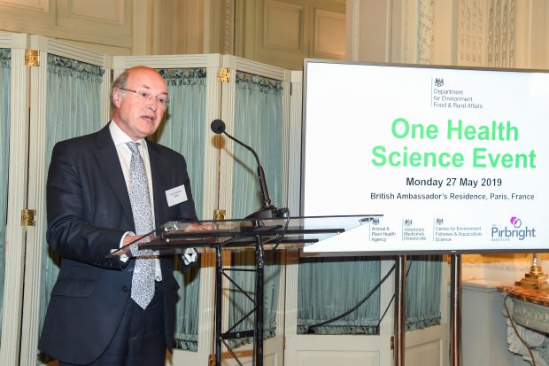 Image of a gentleman in a suit standing at a microphone with a screen behind him showing the words: Department for Environment Food and Rural Affairs, One Health Science Event, Monday 27 May 2019, British Ambassador's Residence, Paris, France.