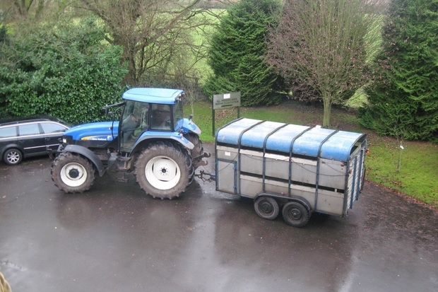 Image of a blue tractor parked on black tarmac towing a large trailer.