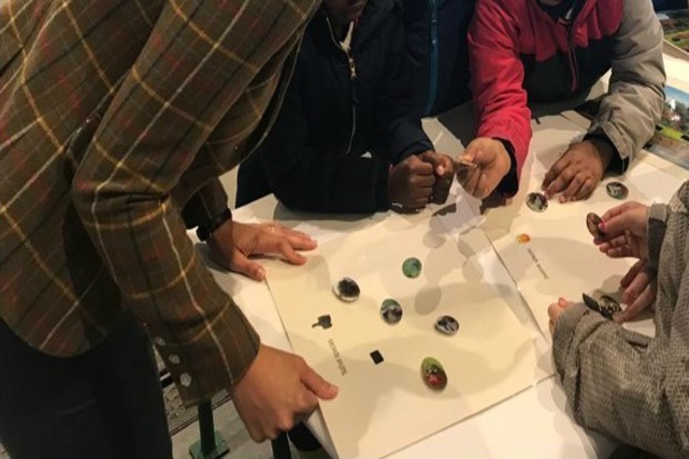 Image of an adult and some children standing around a table with a paper activity in front of them.