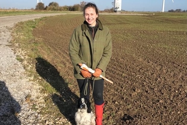 Image of Rowena Hill, standing on a field with a dog at her feet.