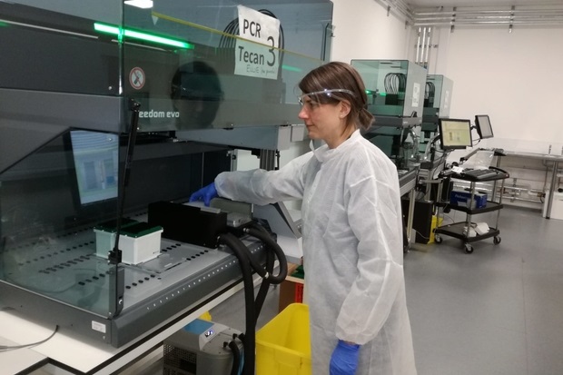 Female scientist wearing goggles, gloves and a white protective suit loading a Tecan PCR machine
