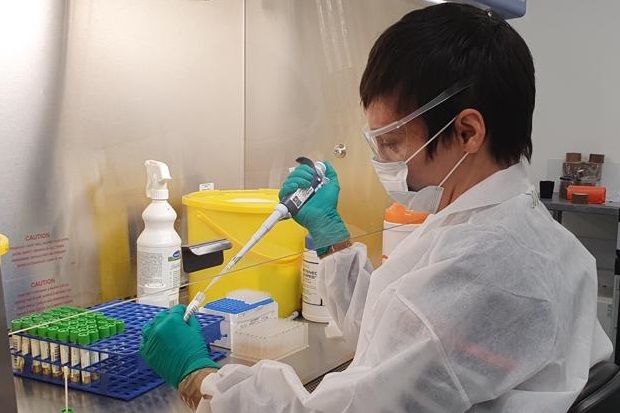 Female scientist wearing a face mask, goggles and white protective suit using a pipette.