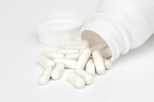 Image of a white bottle of pills spilling white capsules