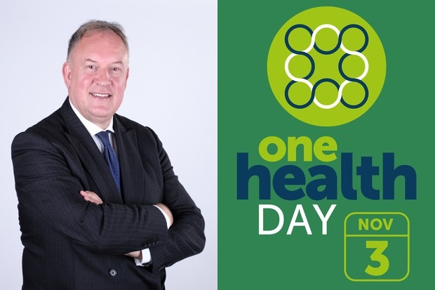 Image of a man in a suit standing with his arms crossed next to the One Health Day logo, November 3