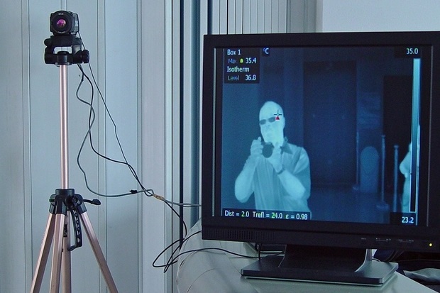 Image of a thermal imaging camera next to a monitor showing a thermal image of a man with a camera.