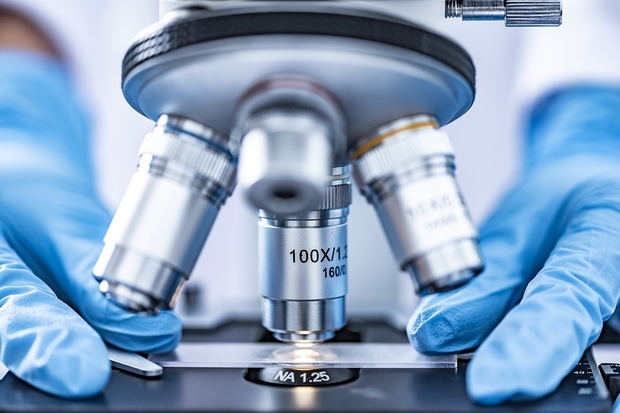 Image of the 4 lenses of a microscope with two blue gloved hands holding a slide below them