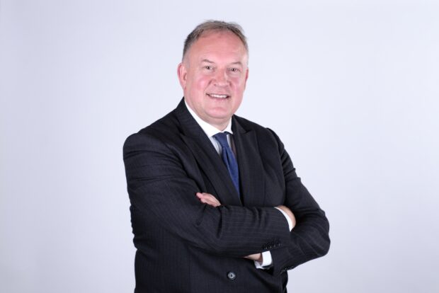 Image of a white man in a suit and tie posing for a photo with his arms crossed.