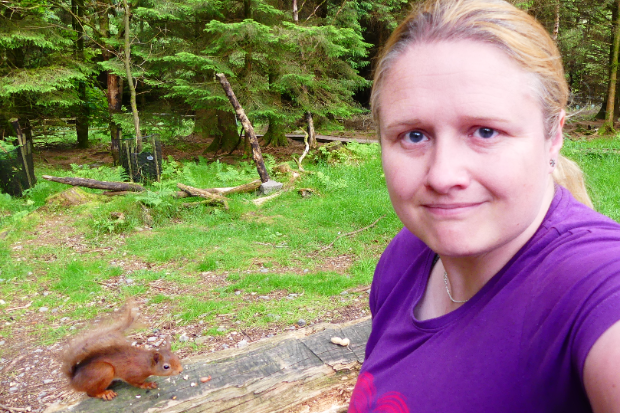 A female standing next to a red squirrel in woodland