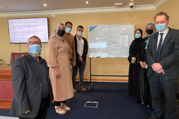 Group of four males and three females wearing facemasks, standing in front of a whiteboard