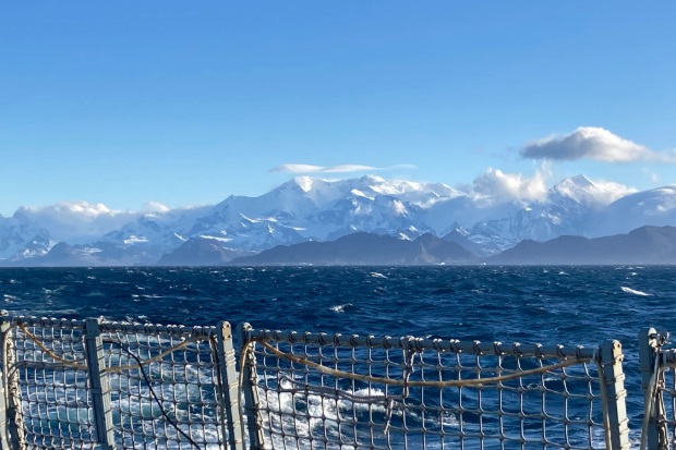 A scenic view from a ship's deck, showcasing the vast ocean and majestic snow-capped mountains in the distance