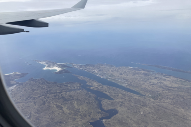 Airplane window perspective revealing a stunning landscape of ocean waves and coastal land