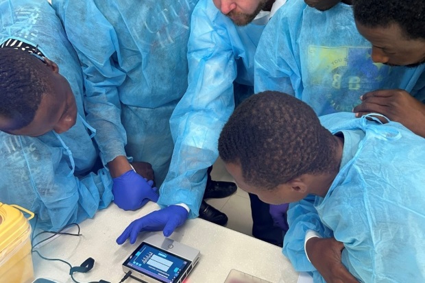 Demonstration of a small table top device to a group of individuals wearing PPE