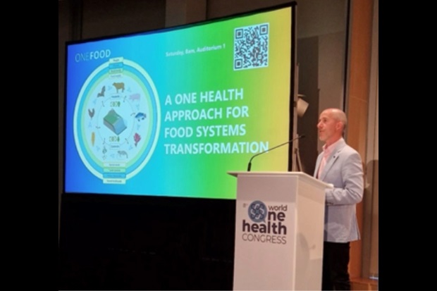 Gentleman at a lectern with a slide beside him entitled, "A One Health Approach for Food Systems Transformation"