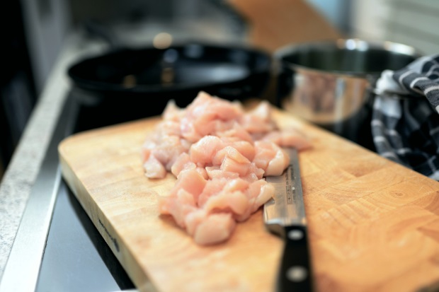 Image of some chopped raw chicken on a chopping board with a kitchen knife.