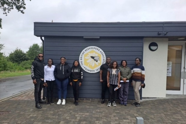 Eight individuals standing outside a grey building with the British Beekeepers Association badge on display on the building's exterior