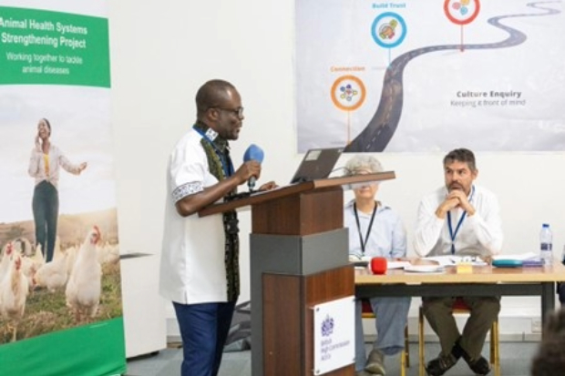 Gentleman speaking into a microphone at a lectern. There are pull-up banners and posters behind him, one which says, "Animal Health Systems Strengthening Project".
