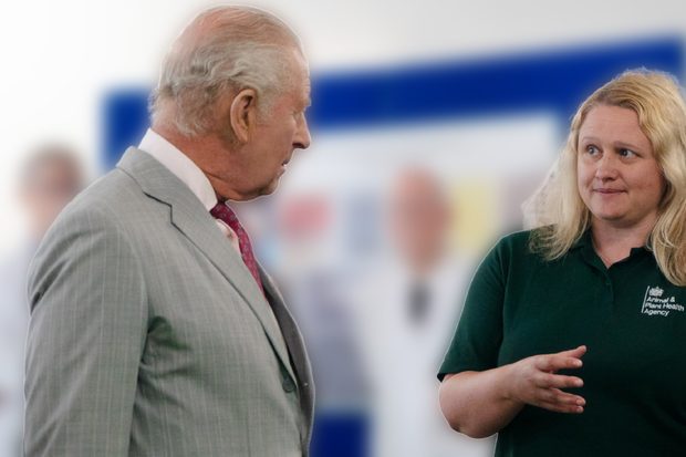 His Majesty The King listens as a female in a green APHA polo gestures as she talks; blurred figures create a calm, attentive atmosphere.